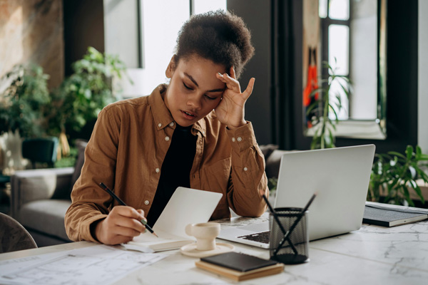 Une jeune femme travaille avec concentration dans un bureau moderne, prenant des notes devant son ordinateur portable.