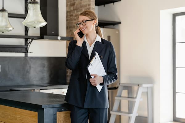 Une agente immobilière professionnelle sourit en tenant une conversation téléphonique dans un bureau moderne, un dossier à la main.